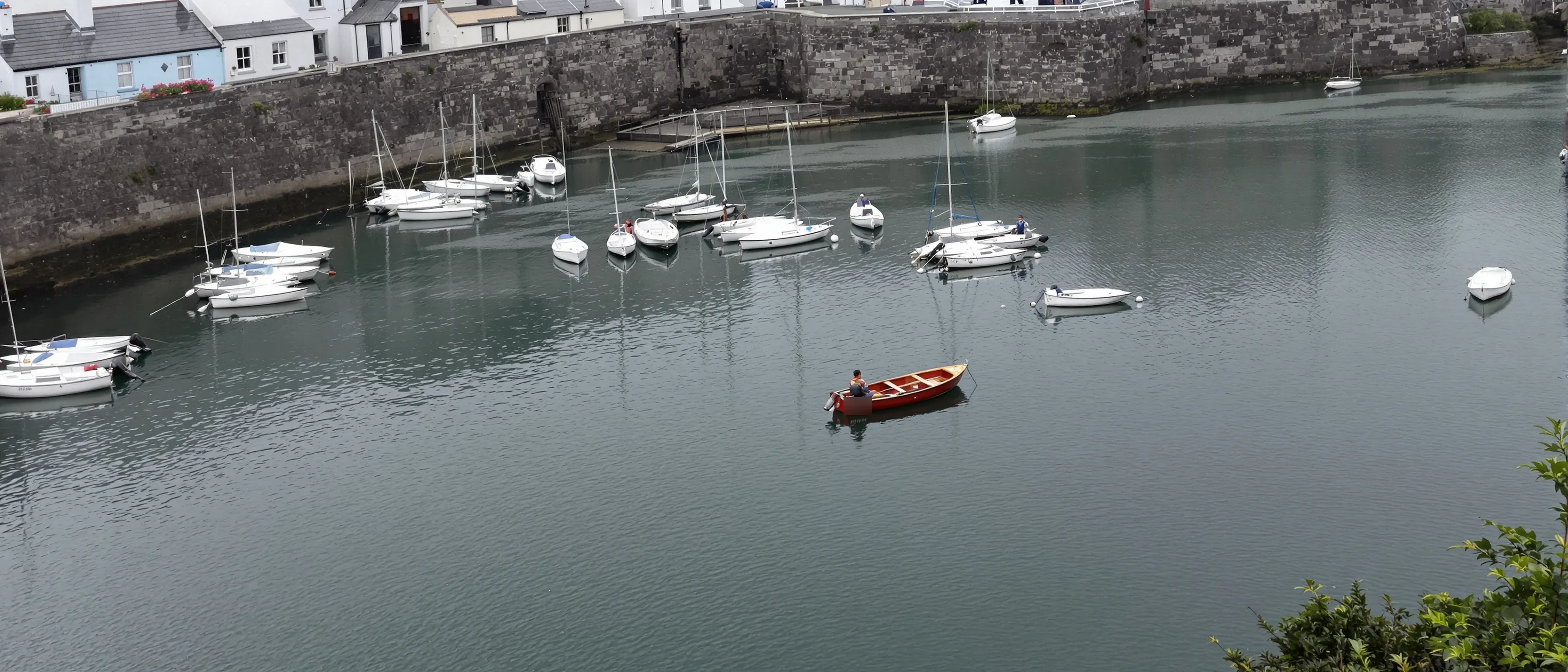 Ein tiefrotes Ruderboot liegt zwischen lauter weißen Booten in einem stillen Hafenbecken.