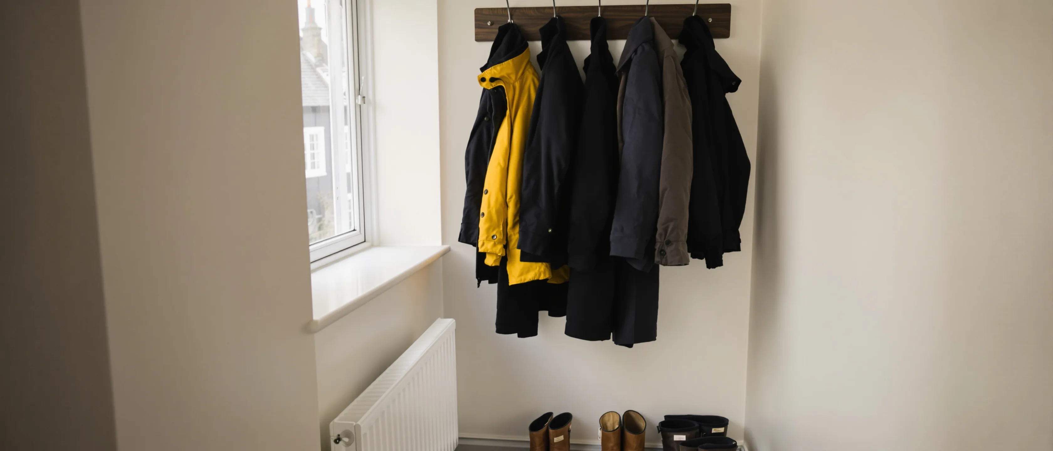 Eine Garderobe mit dunklen Mänteln und einer einzelnen leuchtend gelben Jacke, darunter Schuhe.