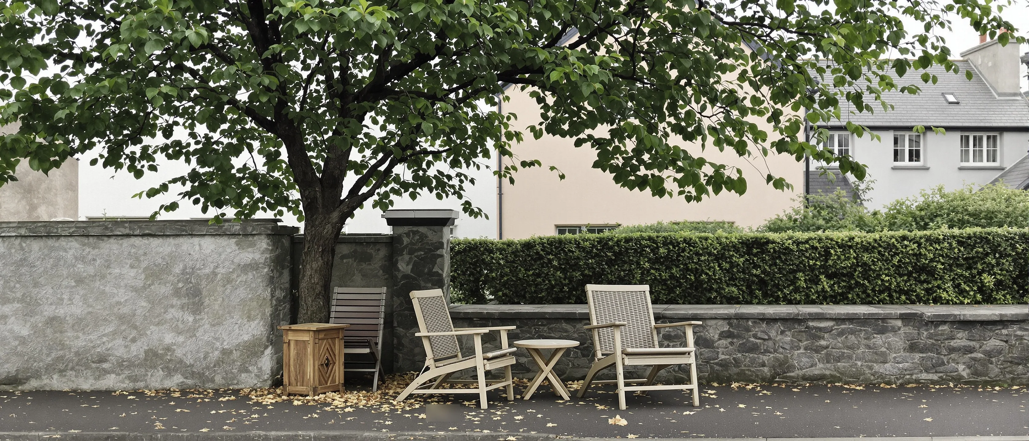 Zwei Gartenstühle nebeneinander unter einem großen Baum an einer Steinmauer, Laub auf dem Boden.