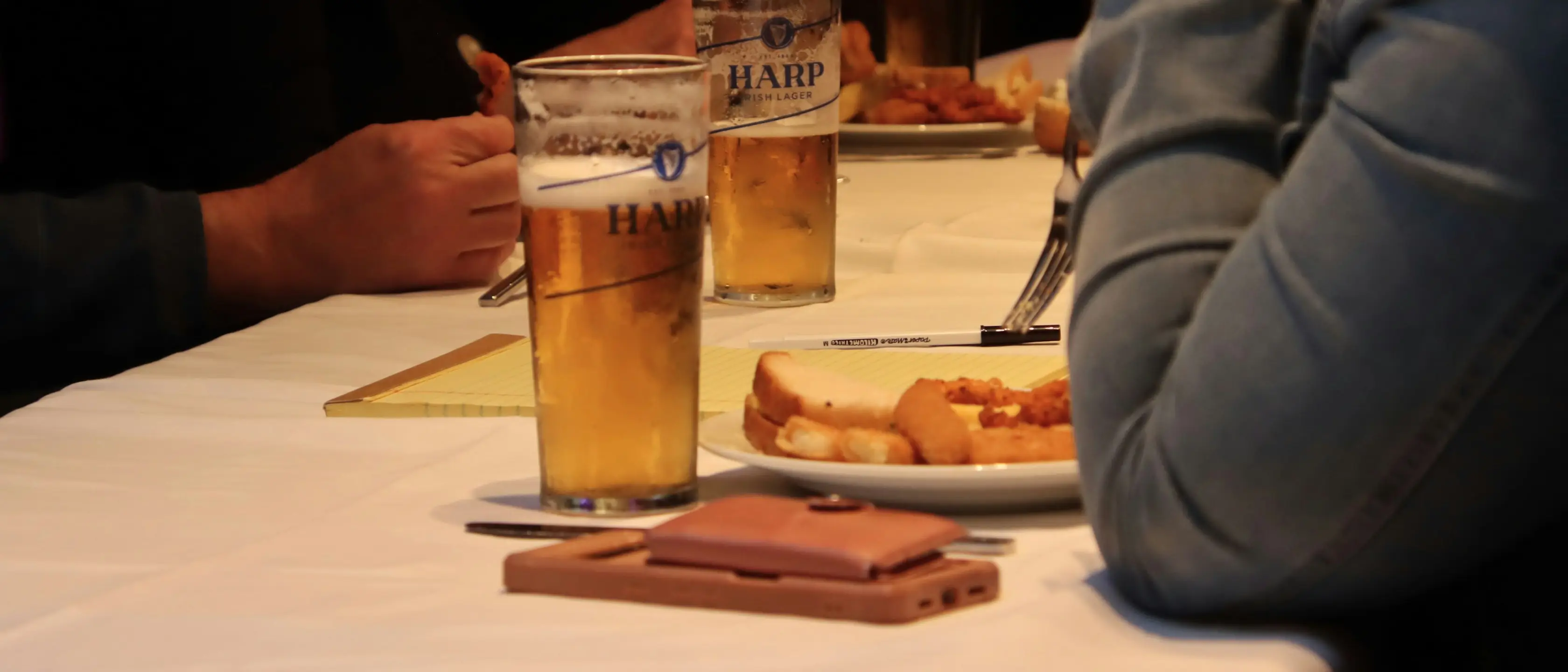 Zwei Gläser Bier und ein Teller auf einem Pubtisch, jemand greift danach.