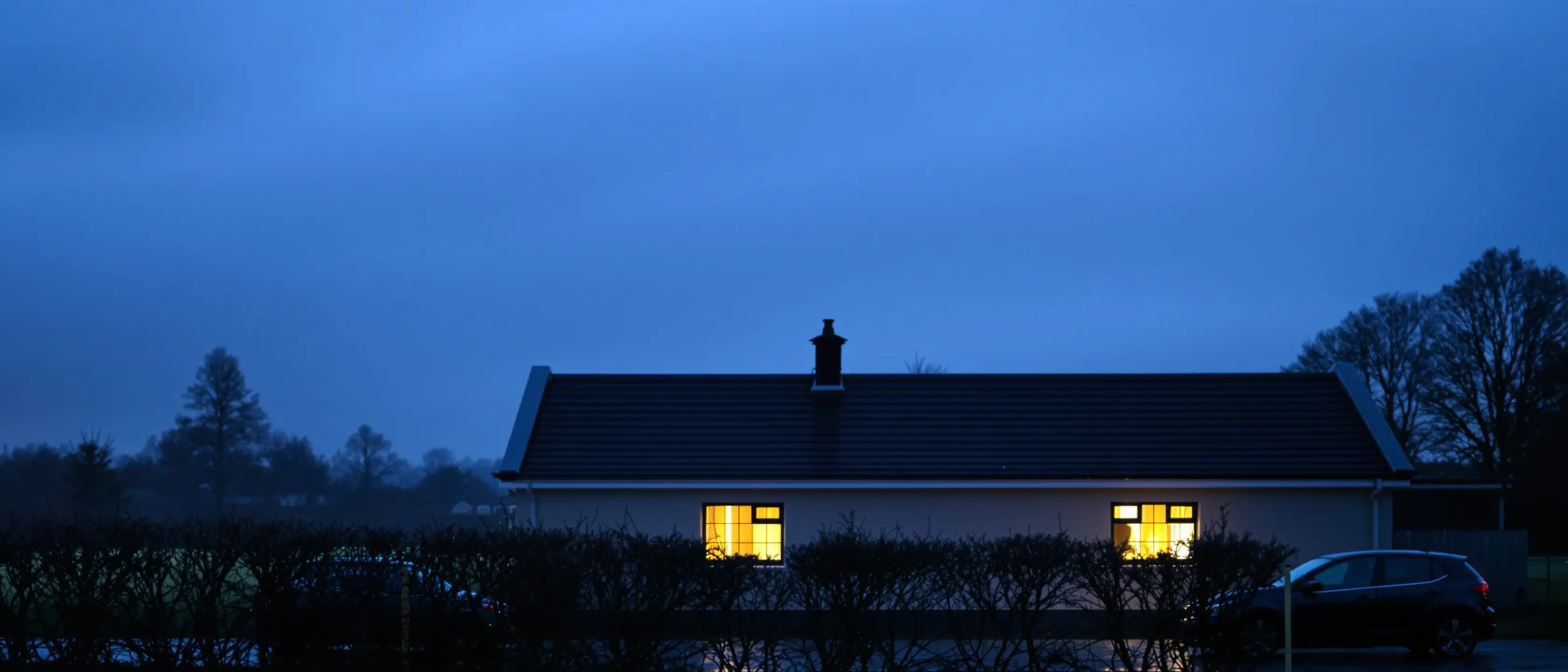 Ein niedriges Vereinsheim am Sportplatz im Winterabend, in zwei Fenstern brennt Licht.