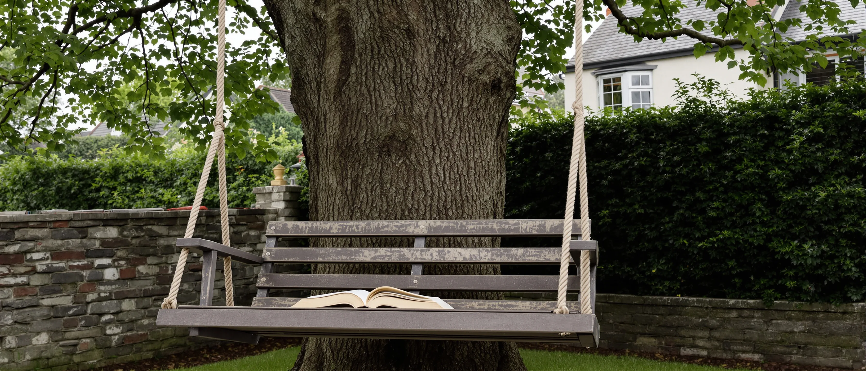 Eine Gartenschaukel an einem alten Baum, auf dem Sitz liegt ein aufgeschlagenes Taschenbuch, geflecktes Licht.