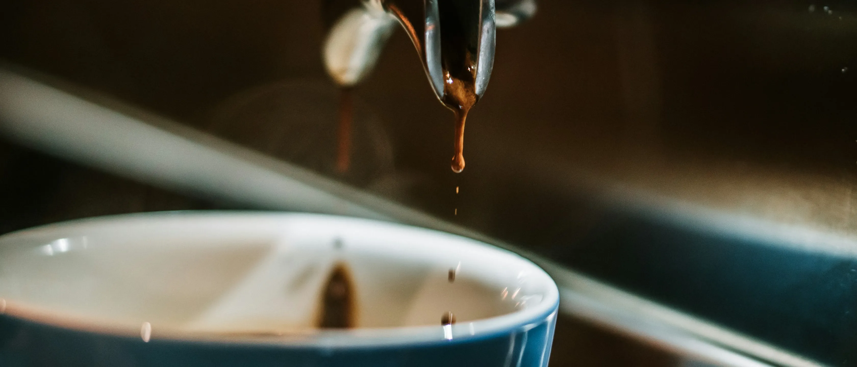 Espresso tropft aus dem Siebträger in eine blaue Tasse.