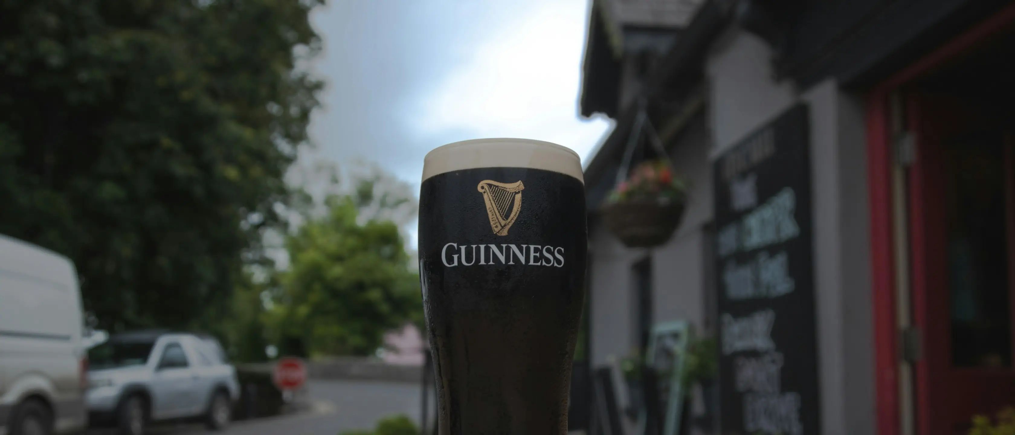 Ein volles Glas Stout auf einem Tisch vor einem Pub.