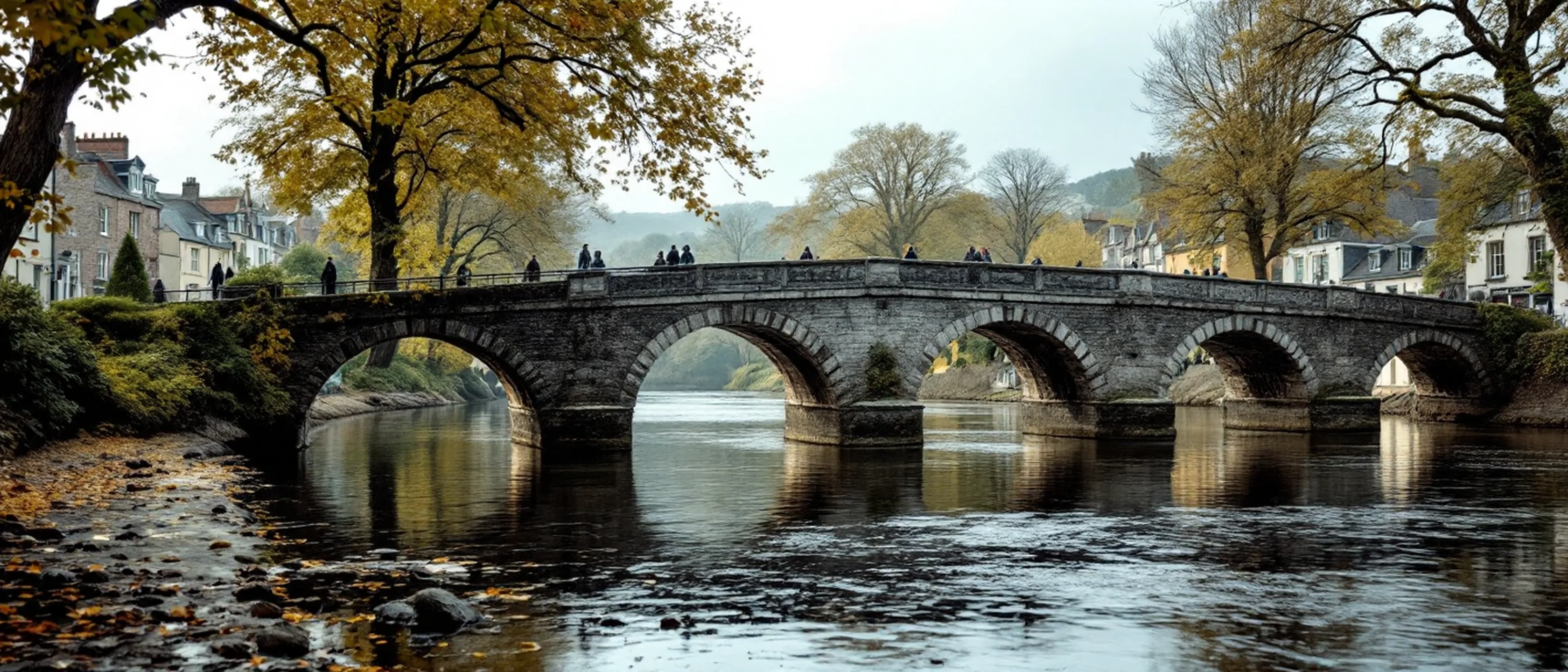 Eine Steinbrücke über einen langsamen Fluss in einer Marktstadt, Bäume an beiden Ufern, stilles Wasser.