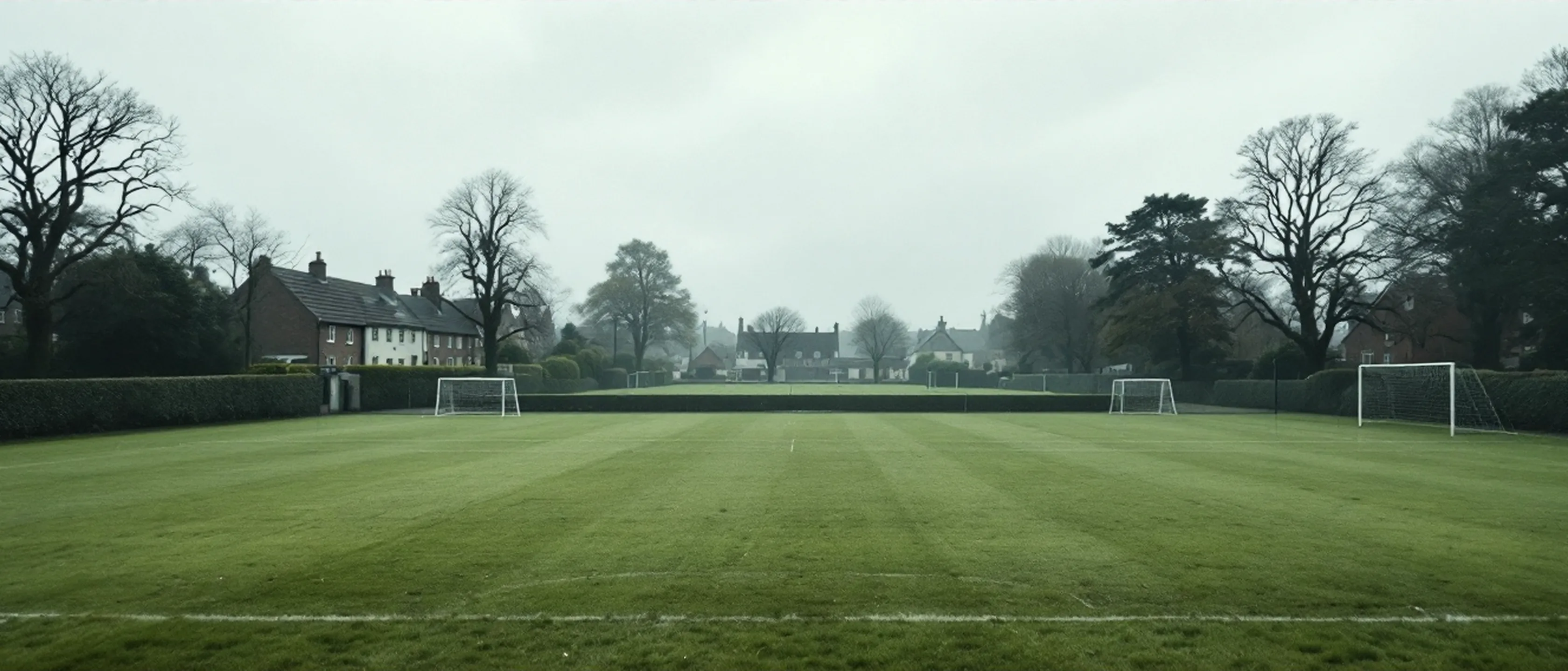 Ein leerer Schulsportplatz in einer irischen Kleinstadt mit Toren, Hecke und Bäumen am Rand, keine Kinder.