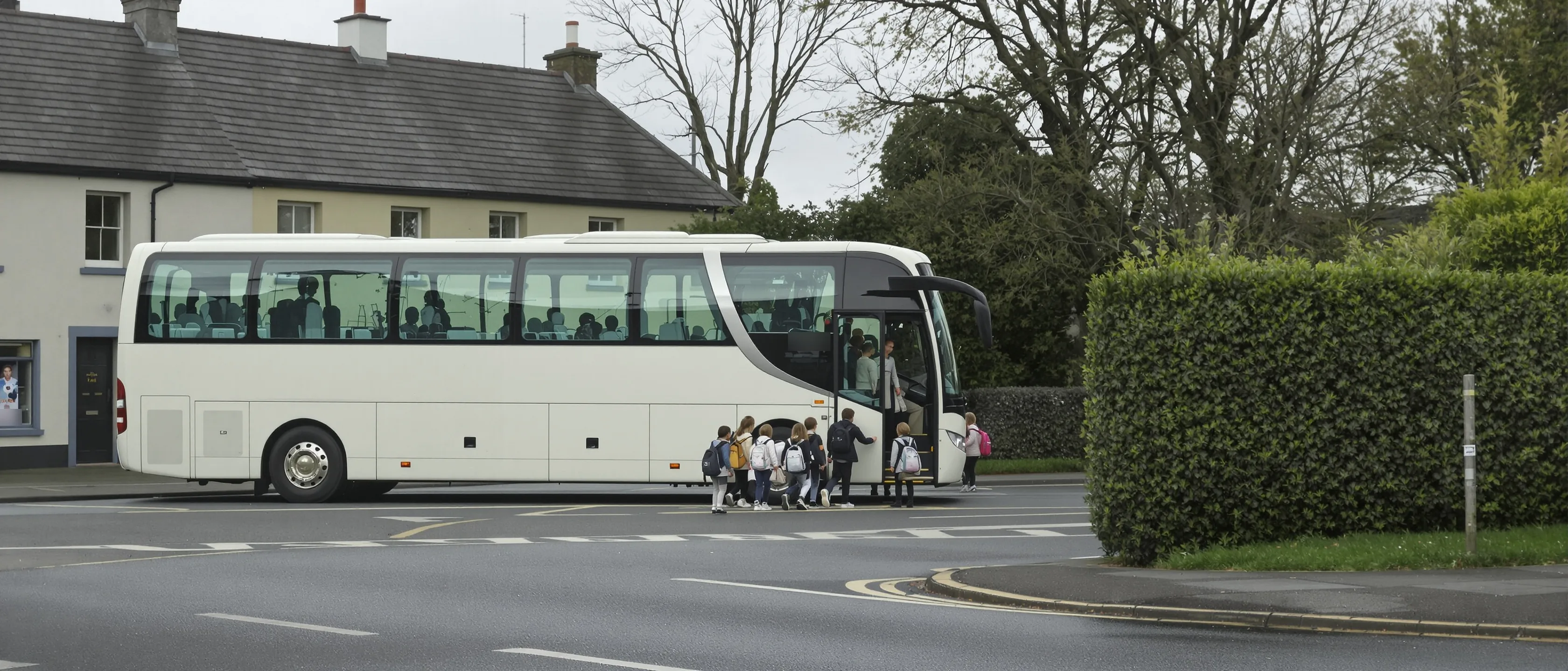 Heller Reisebus wartet an einer Dorfkreuzung, eine kleine Gruppe Kinder mit Schulranzen steigt von hinten gesehen ein.
